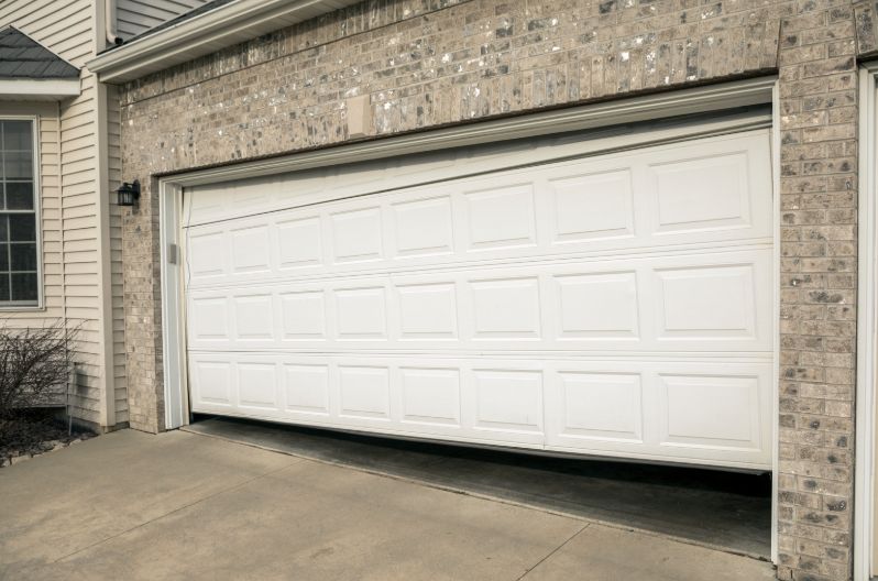 Damaged garage door hanging crooked off its track needing emergency repair in Brownsville
